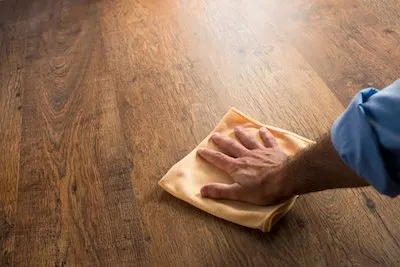 Male hand cleaning and rubbing an hardwood floor with a microfiber cloth.