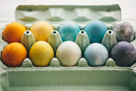 Naturally dyed Easter eggs in carton tray on white wooden background