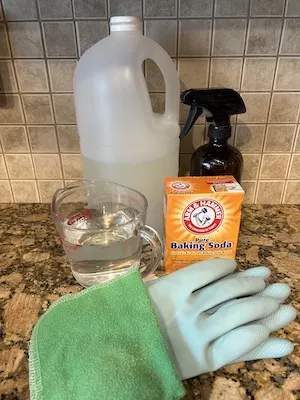 Vinegar, glass spray bottle, water, baking soda, cleaning cloth, and rubber gloves on countertop