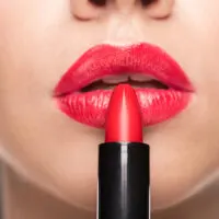 Woman holding tube of dark pink lipstick against her lips