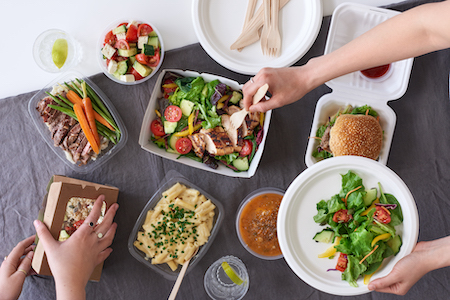 Overhead spread of assorted takeout food with hands serving up