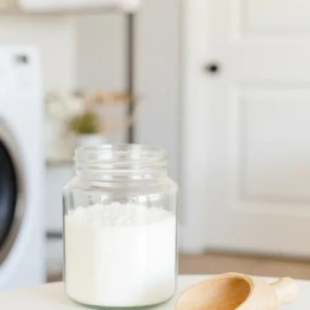 Picture of a clear glass jar filled with homemade laundry scent booster sitting on a table next to a small wooden scoop