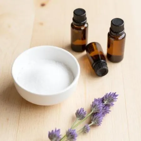 Picture of a bowl of Epsom salt alongside several brown essential oil bottles and lavender sprigs