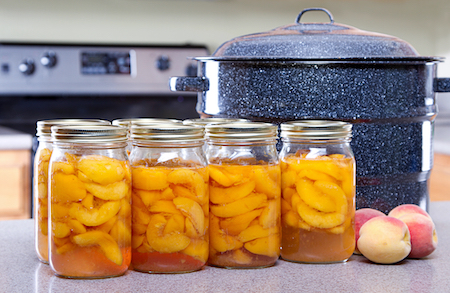 Canned peaches with large pot or canner in a kitchen with fresh peaches in front