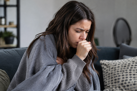 Person coughing while wrapped up under a cozy blanket